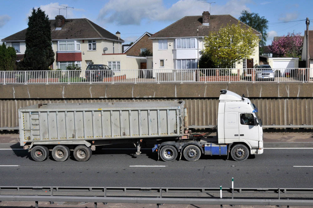 Lorry with large metal container to back driving alongside ridged concrete with metal railings
