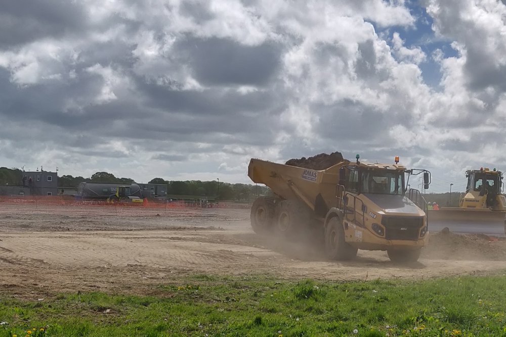 Two large building site vehicles collecting rubble with clouds overhead