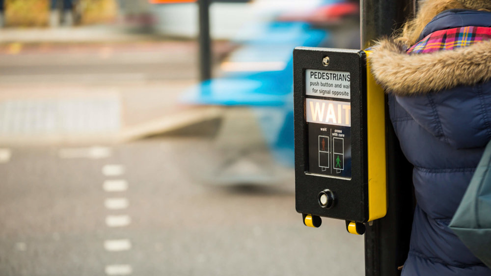 Pedestrian crossing button displaying 'Wait' with person in navy parker coat beside