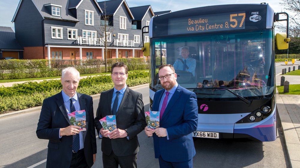 Three men in suits holding brochures in front of blue and purple bus displaying Beaulieu as the destination