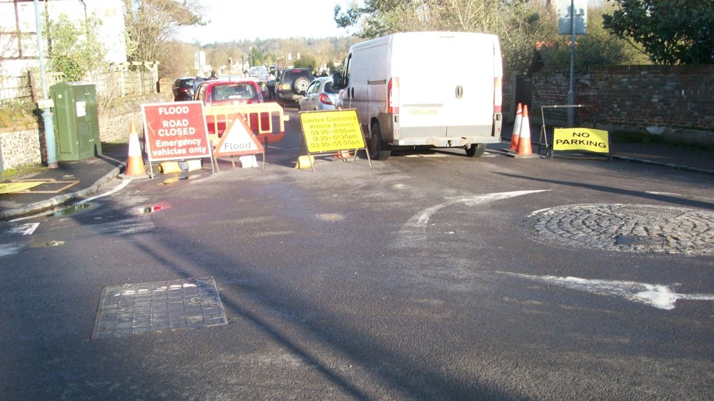 A road that has flooded is being blocked by warning signs and bollards.